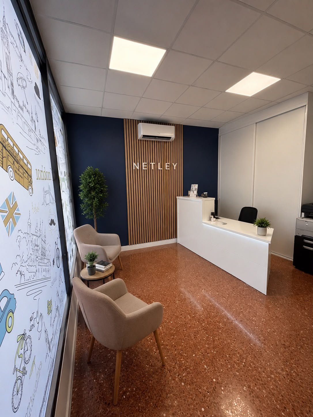 Recepción de Netley Language Studio: el logo en una pared de listones de madera, butacas y una vidriera ilustrada con motivos de Londres.
